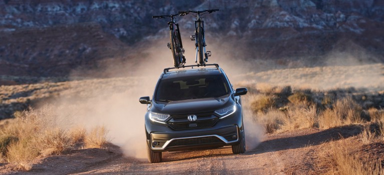 Action shot of CR-V Touring in Crystal Black Pearl driving down a dirt road with dust cloud in desert mountain location.