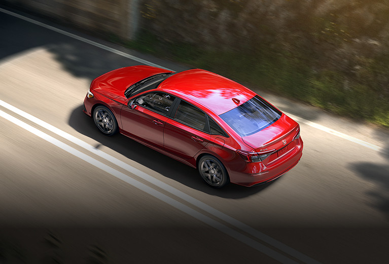 2024 Civic Sedan in Rallye Red driving in a highway passing through a forest