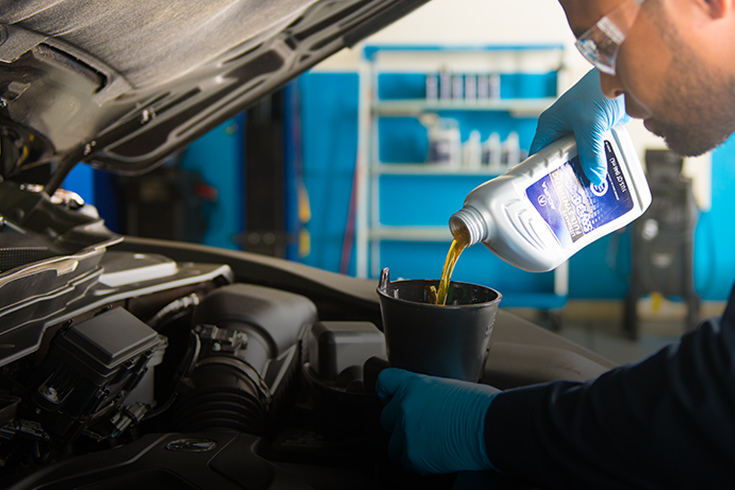 Close up of a mechanic pouring oil into the open engine bay.